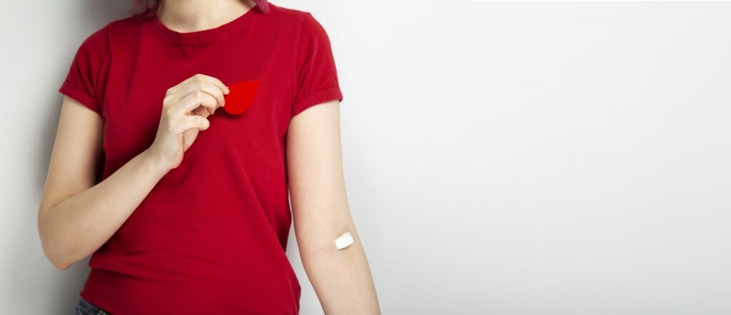 Don du sang - jeune femme en t-shirt rouge qui tient à la main un petit papier en forme de goutte de sang.