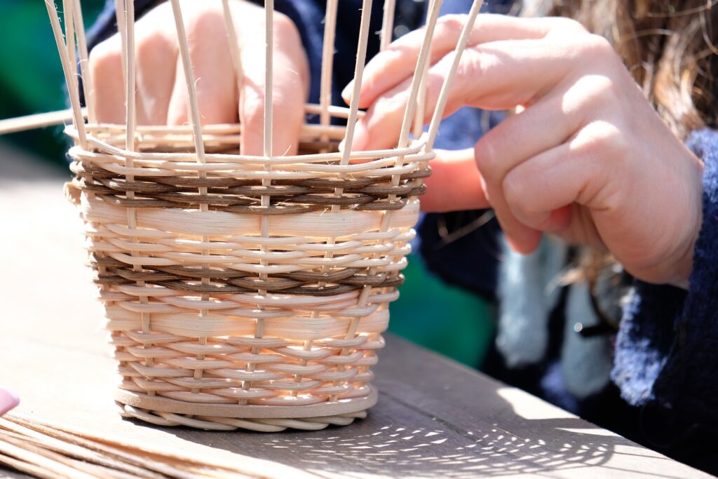 Mains d'une personne qui fabrique un petit panier en osier.